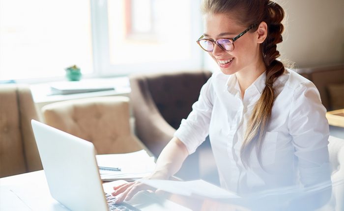 Lady wearing glasses smiling while sitting operating a laptop
